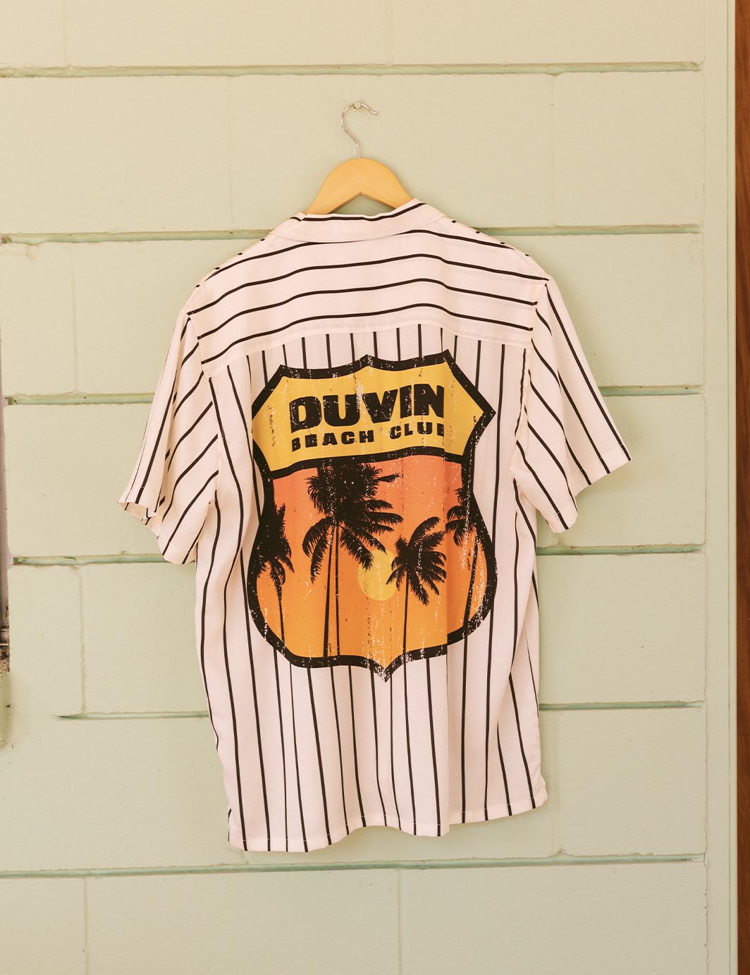 Striped shirt with palm tree design and 'Puvin Beach Club' text on a wooden background