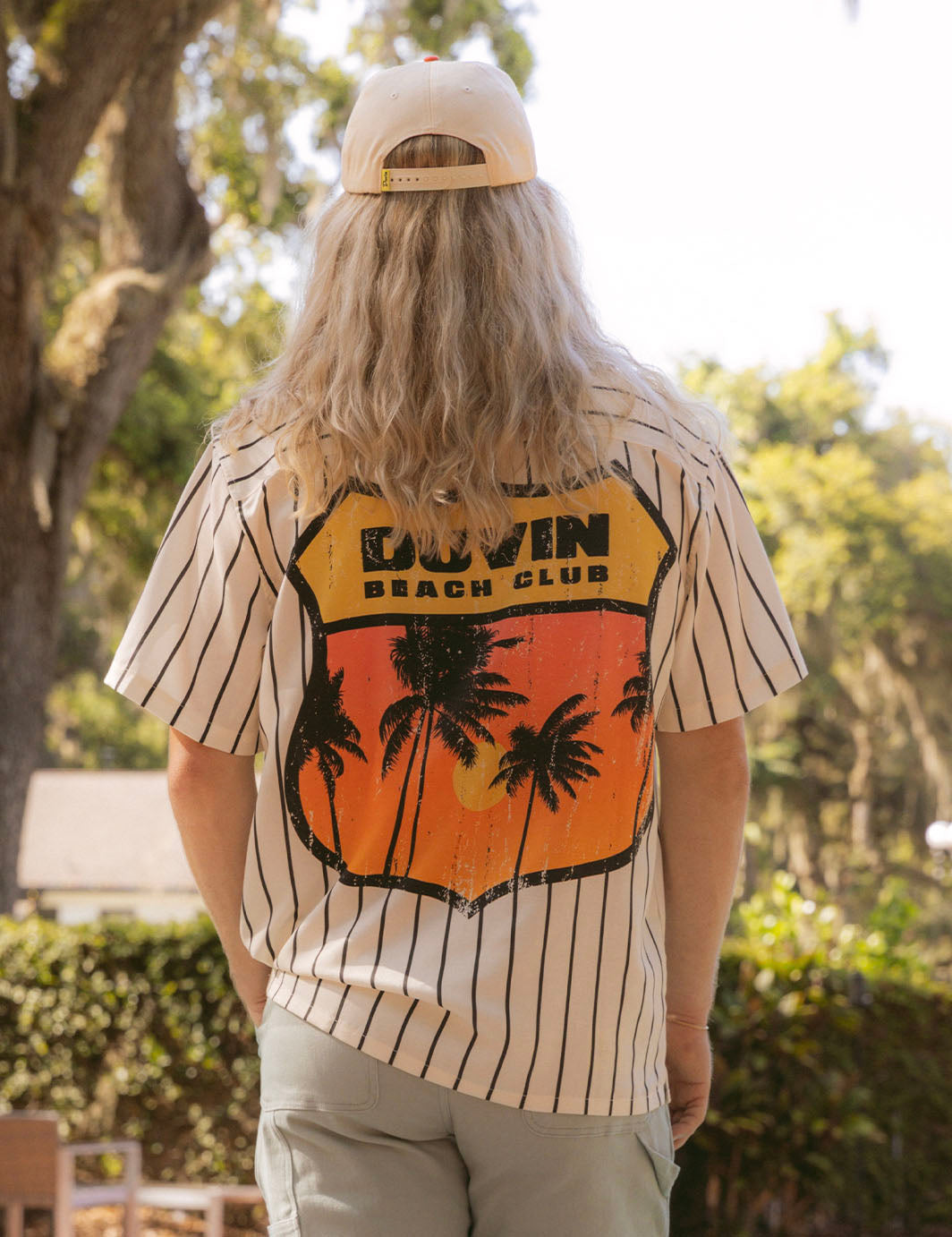 Person wearing a shirt with 'Dovin Beach Club' design outdoors